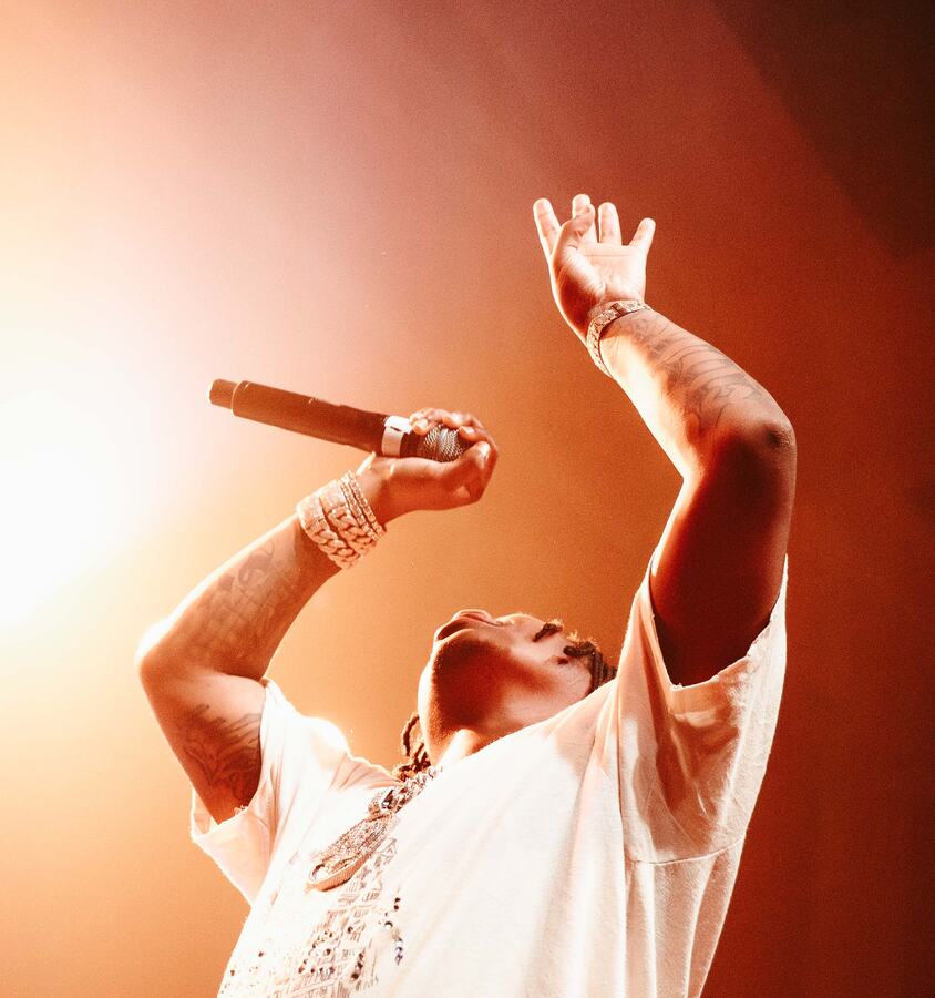42 Dugg performing beneath warm orange stage lights with a microphone raised